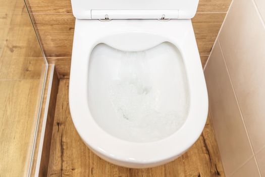 Clean, white ceramic toilet bowl in the bathroom, toilet room. Open toilet with lid. Plumbing, mockup, design template for interior, cleaning, hygiene concept. View from above, flat lay. Bathroom interior
