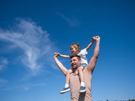 Portrait of happy man holding his little daughter on neck while having rest on summer day