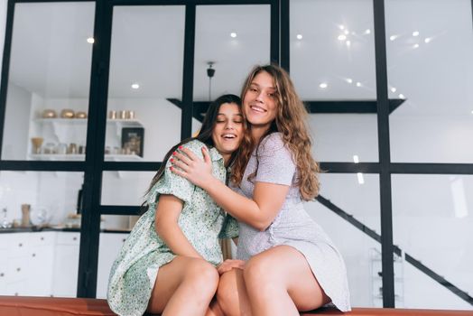 Happy girls embracing at home sitting on a couch in the living room at home