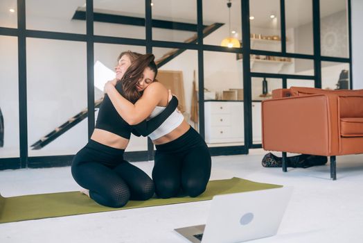 Two girlfriends hug each other after yoga at home