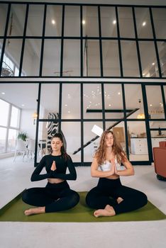 Two young women meditating in lotus pose with hands in namaste. Yoga