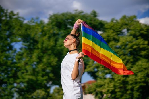 Young woman with lgbt pride flag walking in the park.