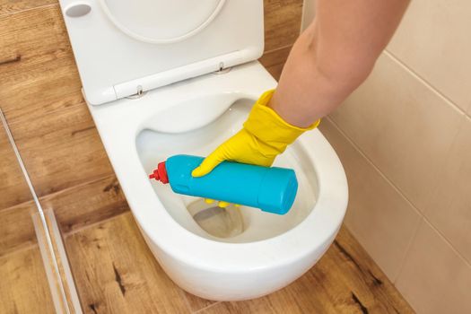 Mockup of plastic blue bottle with toilet cleaner, place for logo. Close-up of female hands in yellow protective gloves using a detergent solution for cleaning, disinfecting and hygienic toilet