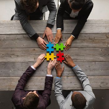 Diverse team people assembling jigsaw puzzle, multiracial group of black and white colleagues engaging in successful teamwork finding business solution, corporate unity teambuilding concept, top view