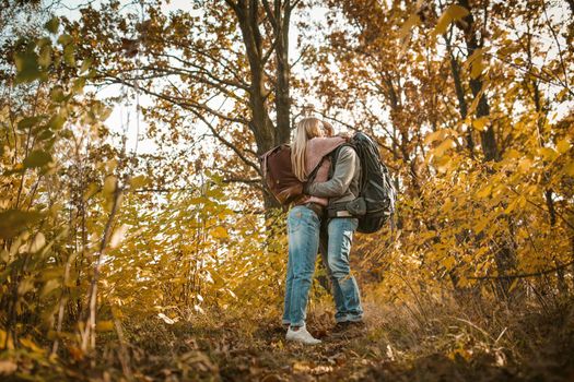 Loving couple of travelers hugs admiring the autumn nature. Young people stand embracing amid multicolor autumn nature. Shot from below. Love and hiking concept.