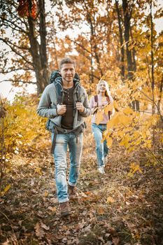 Cheerful Couple Of Backpacker Hiking On Forest Footpath, Man And Woman In Casual Clothing Walking Together In Autumn Nature Outdoors, Focus On Smiling Caucasian Man In Foreground