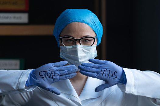 STOP VIRUS Sign On Doctor's Hands In Disposable Gloves, Woman In Blue Medical Uniform Standing Next To The Window, Coronavirus Pandemic, Health Care Concept