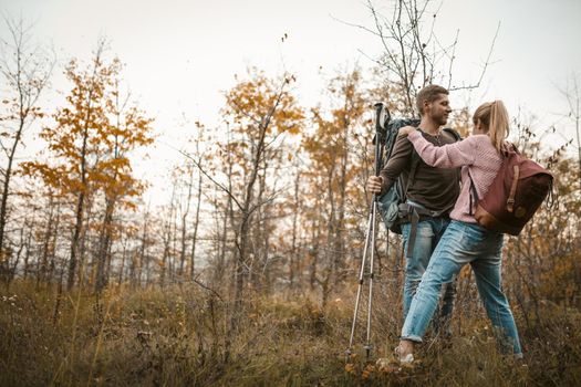 Couple of tourists in love stands embracing leaning on hiking sticks. Young Caucasian man and woman on the background of a young autumn forest. Support concept.
