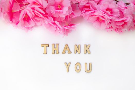 Thank you concept made of wooden letters. Message with pink flower decoration. Text on white background.