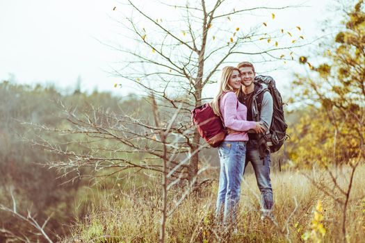 Hugs on top of the hill. Couple of lovers tourists cuddling while looking at the camera. Copy space at left side.