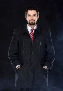 Portrait of fashionable well dressed man with beard posing outdoors looking away, confident and focused mature man in coat standing  on a black background, elegant fashion model.