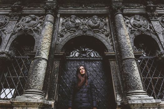 The young girl stands on the background of the old gothic wall.