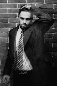 Portrait of fashionable well dressed man with beard posing outdoors looking away, confident and focused mature man in coat standing on a brick wall background, elegant fashion model.