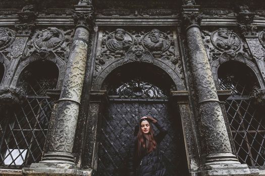 The young girl stands on the background of the old gothic wall.