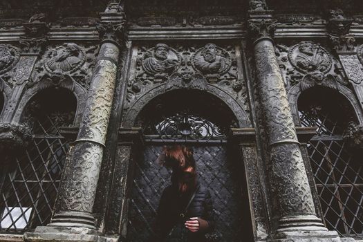 The young girl stands on the background of the old gothic wall.