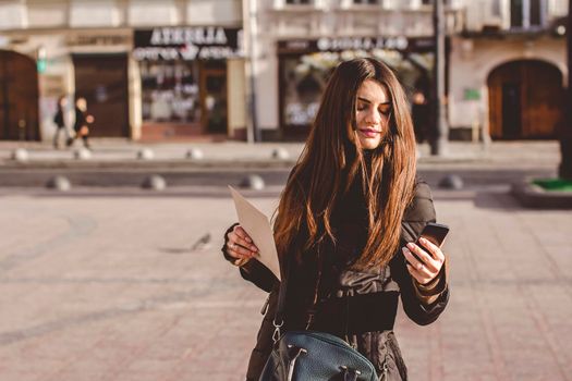 Young nice girl looks at the phone in the middle of a big city.