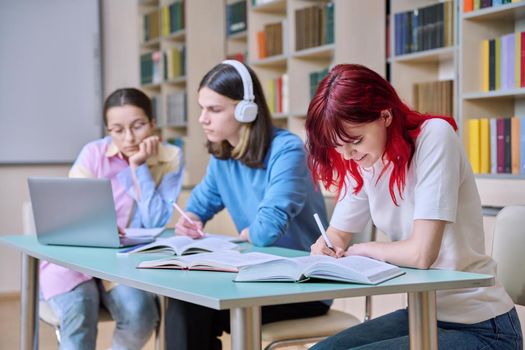 Group of teenage students study at their desks in library class. Teen students writing in notebooks using books laptop. Education, knowledge, high school, college concept