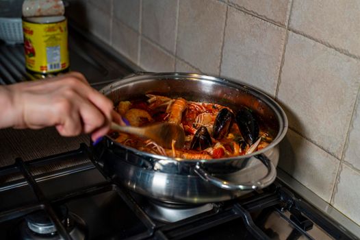 Man handling fish soup with wooden ladle while cooking