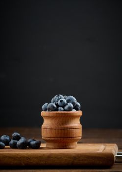 Ripe blueberries in a wooden bowl on the table, black background