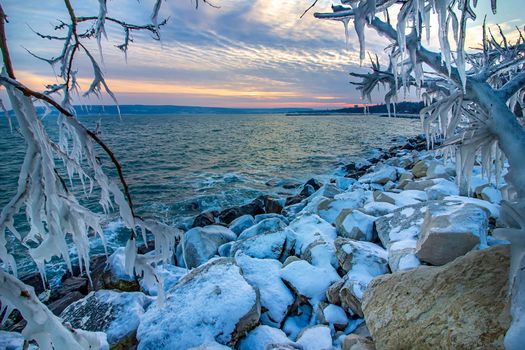 Afternoon at a shore between icicles on tree branches frozen. Winter landscape 