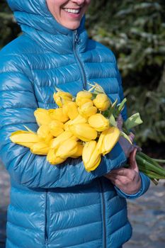 woman in a bright blue jacket with a bouquet of yellow spring tulips, mother's day gift. High quality photo