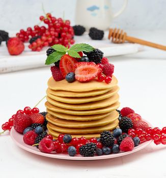 Stack of baked pancakes with fruits in a round plate on a white table