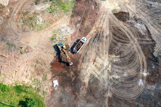 Aerial top view of excavator and dump trucks working at the construction site