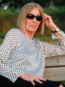 senior lady relaxing in the park wearing sunglasses near the river bank in summer