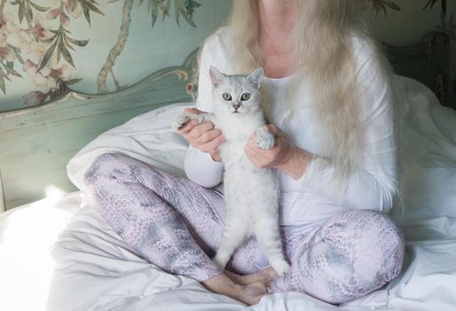 a middle-aged woman with long blond hair meditates in the morning in bed with a kitten,