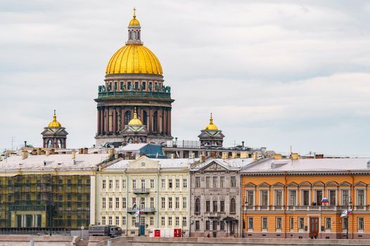 The huge golden dome of St. Isaac's Cathedral through the roofs of houses on the embankment of the Neva River in St. Petersburg in cloudy weather. High quality photo