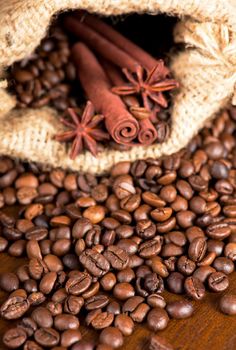 Coffee beans, two cinnamon sticks and anise stars are scattered on a wooden table. copyspace.