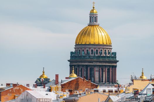 The huge golden dome of St. Isaac's Cathedral through the roofs of houses on the embankment of the Neva River in St. Petersburg in cloudy weather. High quality photo