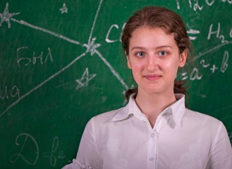 Student girl standing near clean blackboard in the classroom.