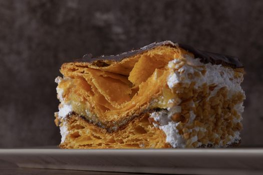 close-up of a chocolate-covered puff pastry with cream and almonds, on a white plate on a dark background