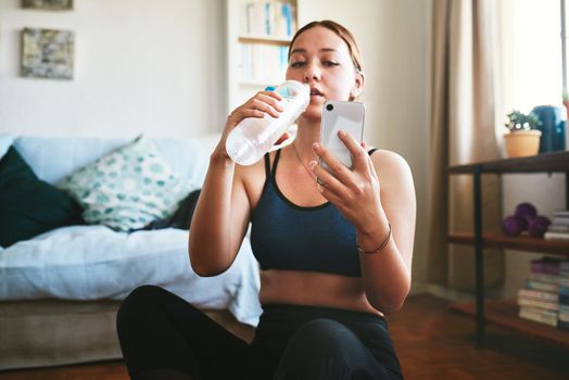 Quick water and social media break. an attractive young woman sitting and drinking water while using her cellphone after a workout