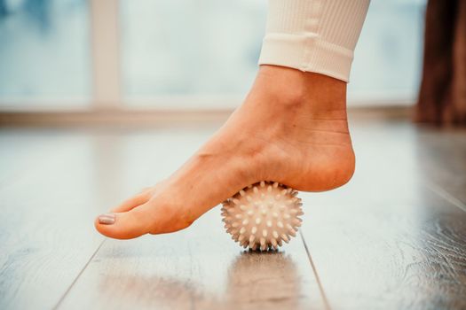 Athletic slim caucasian woman doing thigh self-massage with a massage ball indoors. Self-isolating massage.