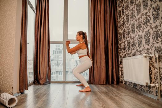Middle aged athletic attractive woman practicing yoga. Works out at home or in a yoga studio, sportswear, white pants and a full-length top indoors. Healthy lifestyle concept.