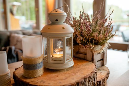 Golden lantern with burning candle inside it standing on festive table decorated by violet cloth and flowers on background. Decor. Wedding
