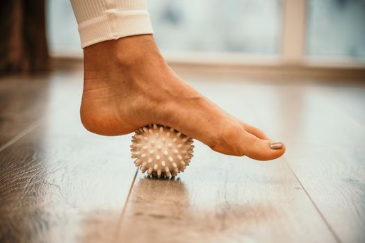 Athletic slim caucasian woman doing thigh self-massage with a massage ball indoors. Self-isolating massage.