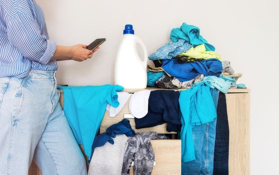 Close-up of a woman in a blue shirt picking up dirty laundry. Phone in hand. white bottle mockup, label, logo. drawing of gifts and prizes, advertising game, marketing from cleaning products