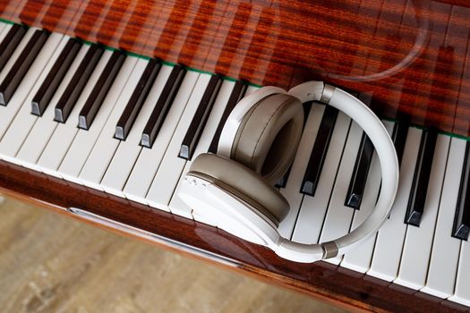 Close-up, white headphones lie on the piano keys. View from above. The concept of modern technology and classical music.