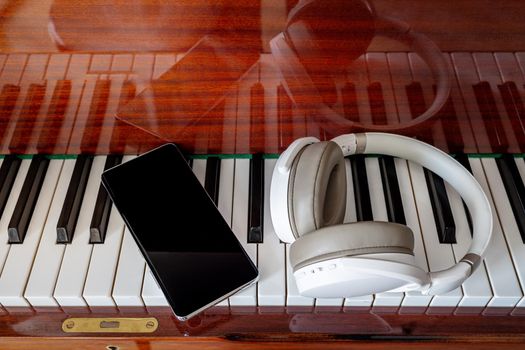 Close-up, headphones, a smartphone lie on the piano keys, top view. The concept of modern education. Online music learning, new hobby. Composing music on a classical instrument using new technologies