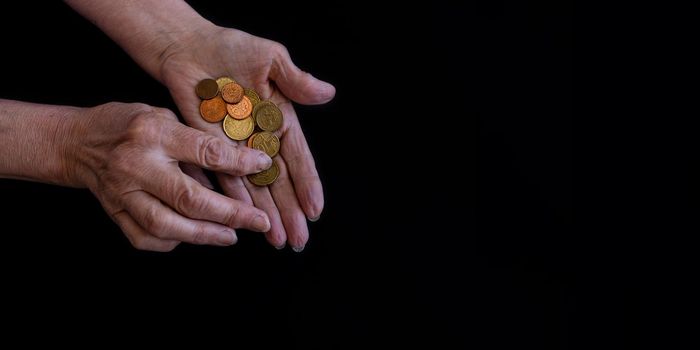 Close-up, on a black background, the hands of an old woman counting coins in her palms. the concept of poverty, old age, economic and financial crisis. Small allowances for pensioners.