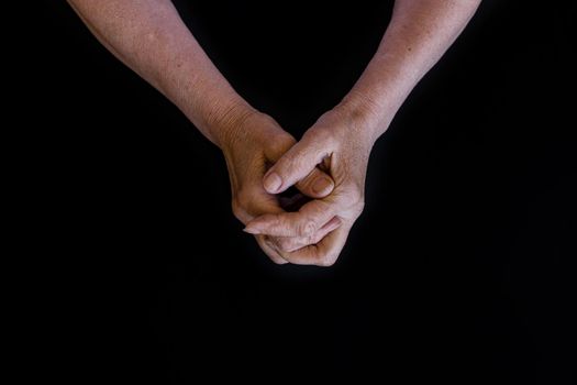 close-up, flat lay on a black background. The hands of an old, wrinkled, white woman are clasped together. The concept of retirement age, old age, loneliness. arthritis and health and joint problems