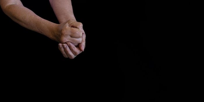 close-up, flat lay on a black background. The hands of an old, wrinkled, white woman are clasped together. The concept of retirement age, old age, loneliness. arthritis and health and joint problems