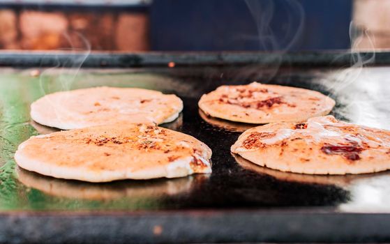 Traditional grilled cheese pupusas, Close up of four traditional handmade pupusas on the grill. Traditional Nicaraguan pupusas with melted cheese on a grill
