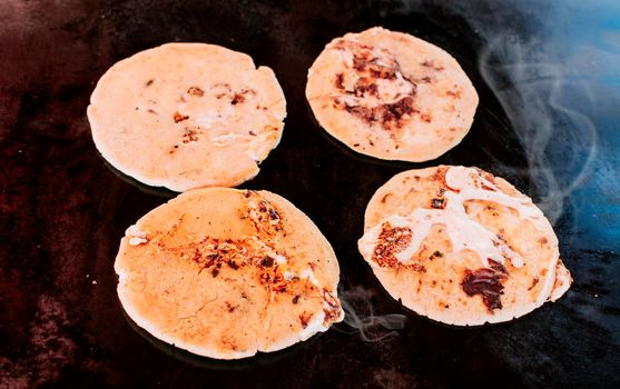 Traditional grilled cheese pupusas, Top view of four traditional handmade pupusas on grill. Traditional Salvadoran pupusas with melted cheese on a grill.