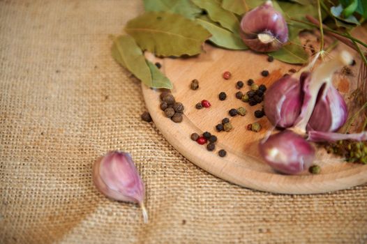 Selective focus on various peppercorns, near bay leaves and garlic cloves on a wooden chopping board. View from above. Still life with food. Fragrant culinary ingredients for preparing pickle and meal