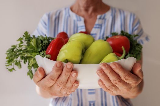 Close-up, an elderly Caucasian woman holds a large plate of vegetables in her hands. The concept of proper nutrition for the elderly, fiber, natural vitamins and trace elements. Right lifestyle