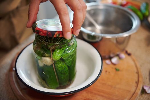 Close Up of hand of housewife putting a sterilized lid on a glass jar with freshly pickled cucumbers. Making homemade pickles for the winter. Pickling. Marinating. Canning. Traditional family recipe